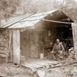 In the summer of 1889, the man sits quietly on the weathered porch of his cabin in Eagle Creek, Murray, Idaho.