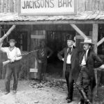 In the late 1800s, the owner of a bar in Idaho stood proudly for a photograph, rifle in hand, embodying the rugged spirit of the American frontier.