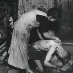 This powerful photograph by Bill Brandt, taken in 1937, features a stark yet intimate scene of a coal miner being bathed at home in Chester-Le-Street, Durham, England.