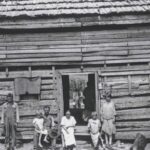 In 1930, a powerful photograph captured a family of sharecroppers standing outside their humble one-room cabin in Troup County, Georgia.