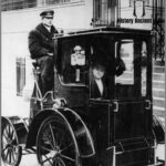 In 1910, a female passenger in a taxi cab in New York captured a moment of elegance amidst the vibrant chaos of early 20th-century urban life.