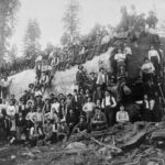 In 1901, the Joe Clark logging team posed beside an enormous “California Sequoia” log, capturing a moment of industry and nature’s grandeur.